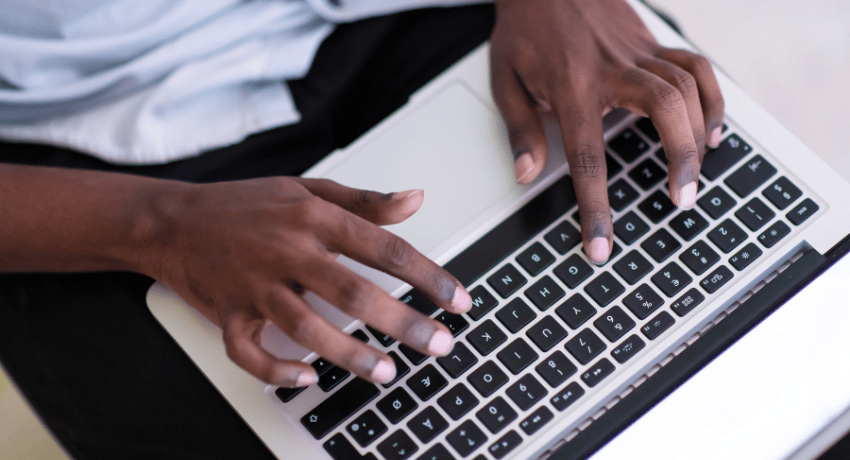 A man's hands type on a laptop plaed on his knee