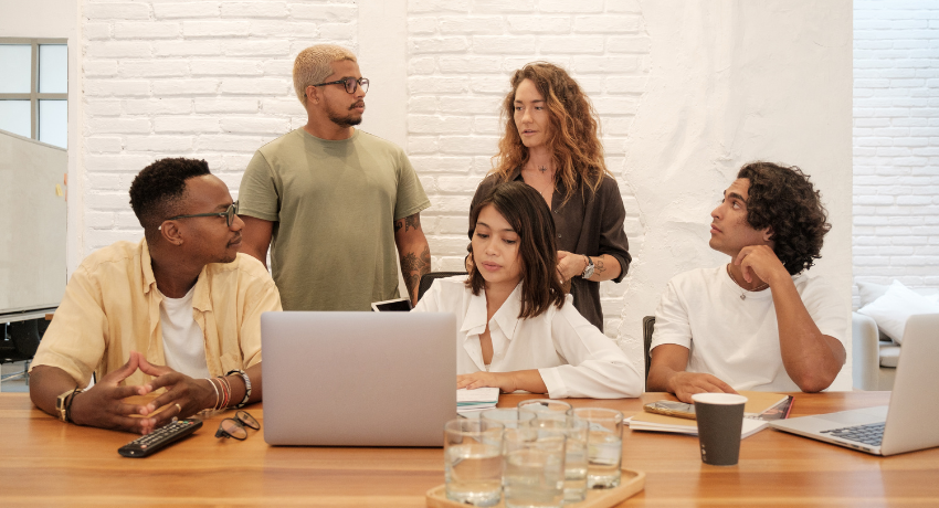 Improving Inclusivity and Accessibility in Digital Learning -  a diverse group of people sat around a desk with laptops, two people are standing