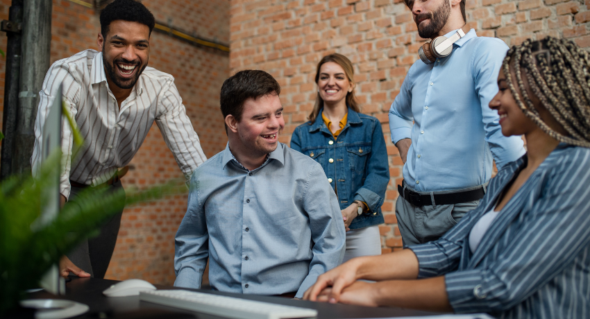 Improving Inclusivity and Accessibility in Digital Learning - a diverse group of people sit and stand around a desk smiling