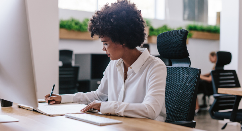 What Is an LMS (Learning Management System) and How To Choose One - Woman sits at desk writing on paper with computer in front of her