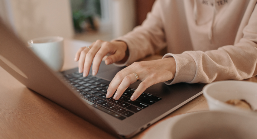 Your Guide To Learning Platforms - person sat at desk typing on laptop with a mug next to her