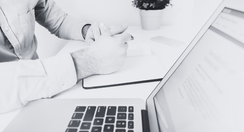 man taking hand-written notes while on laptop