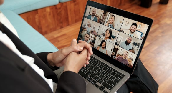 person sits with laptop on knee taking part in a live online class. There are 9 other people in the video call.