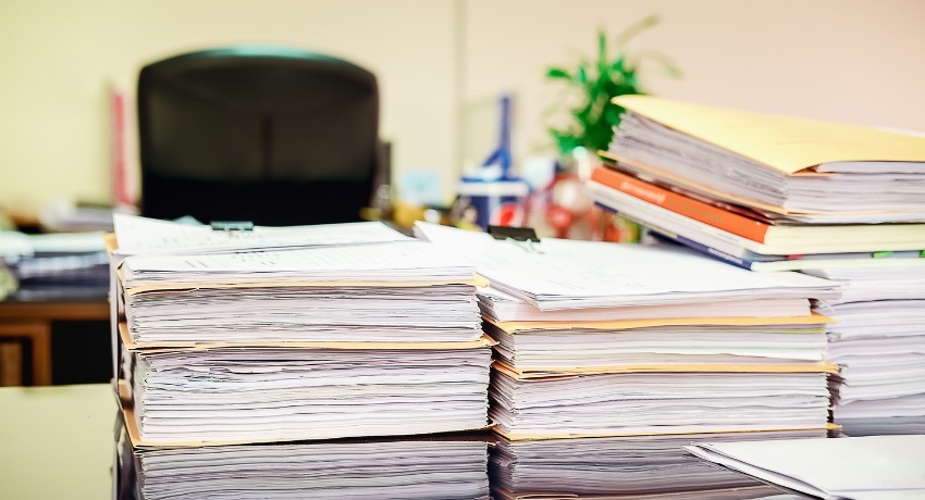 piles of paper and files sit on a desk