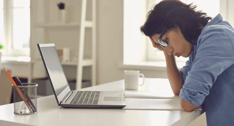 woman sits at laptop with her head in her hands